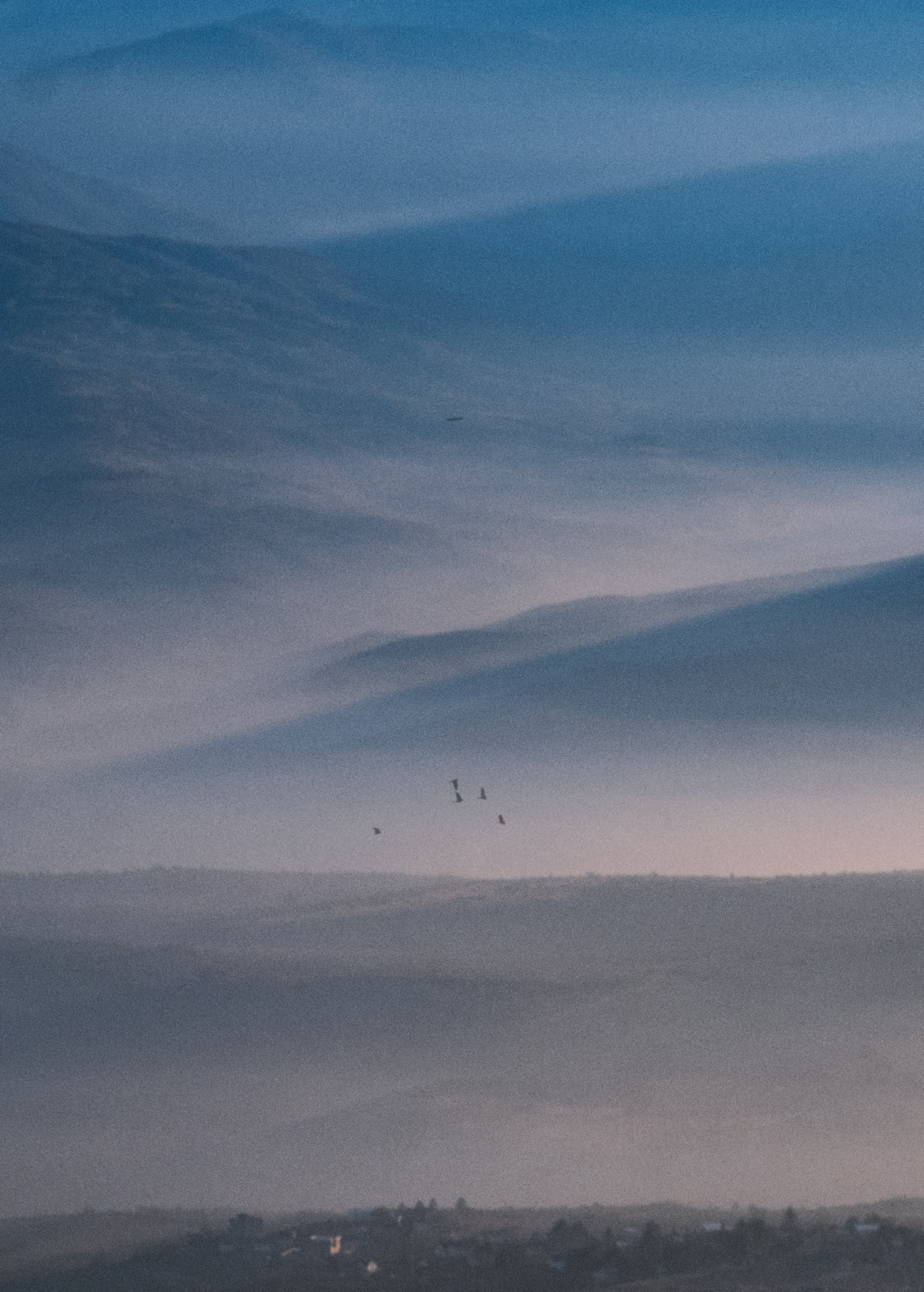 Hazy hills at dusk with birds over the valley