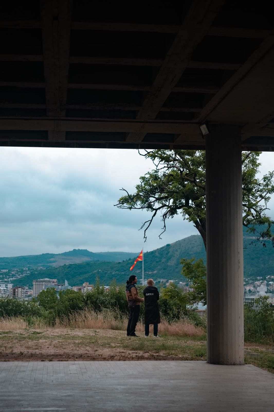 Two figures under a concrete canopy above a valley