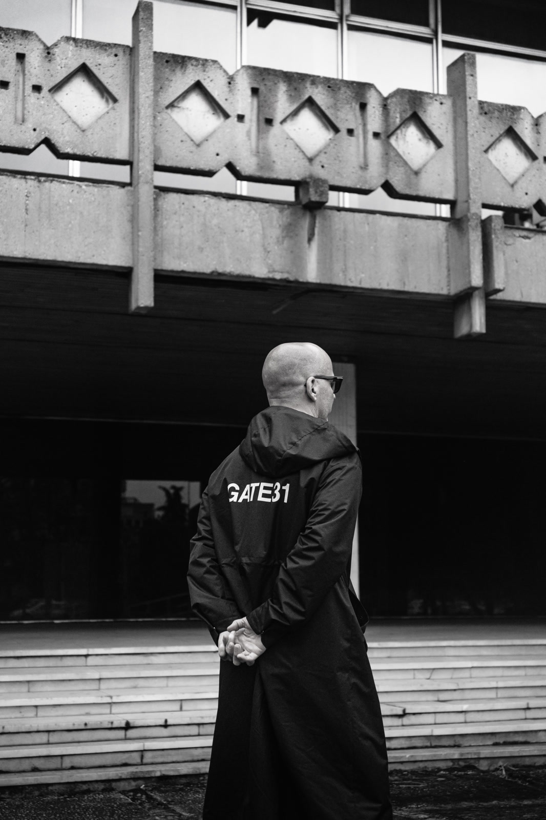 Figure in a long coat beneath a concrete bridge