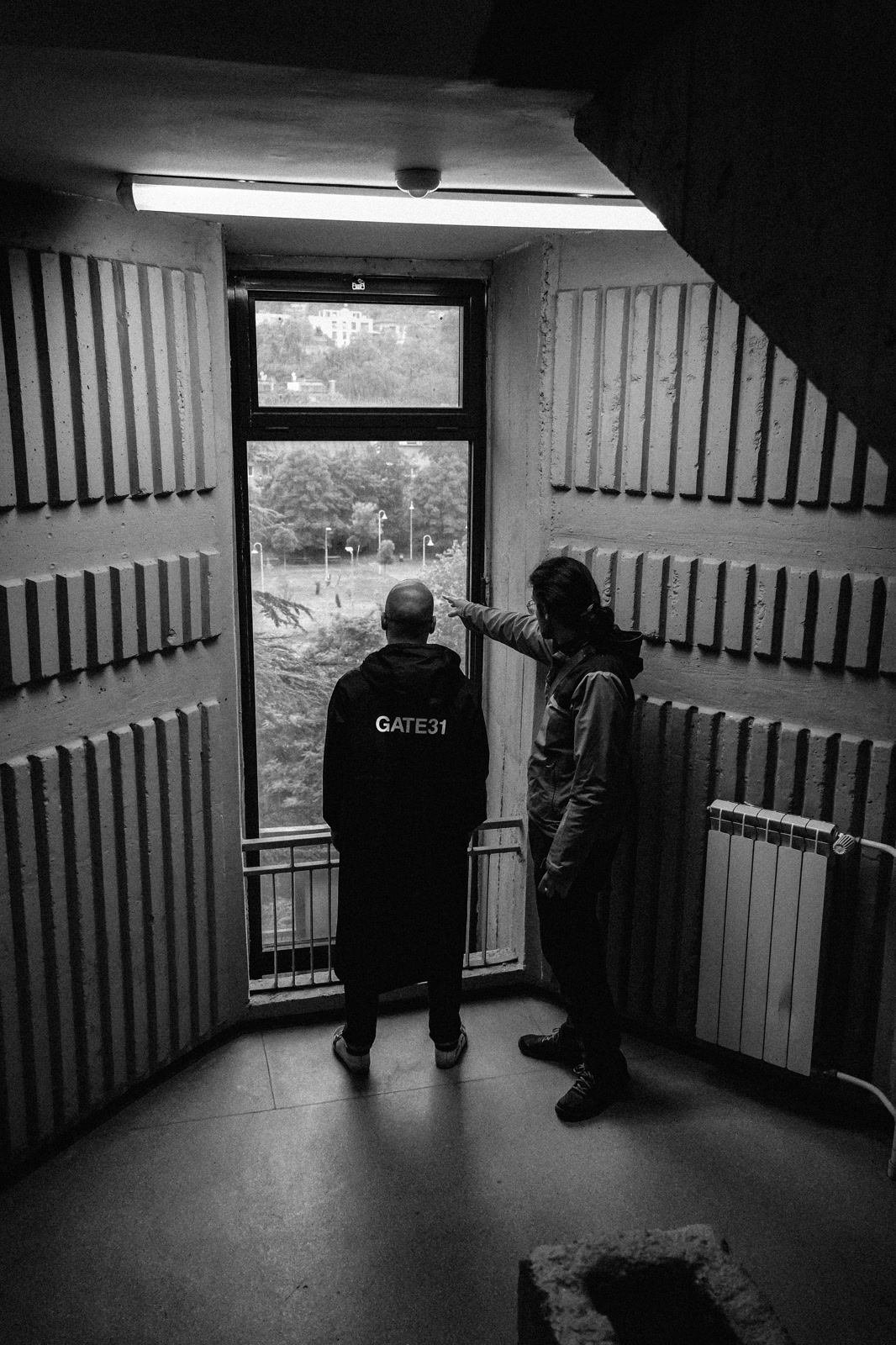 Two figures at a doorway in a bare corridor